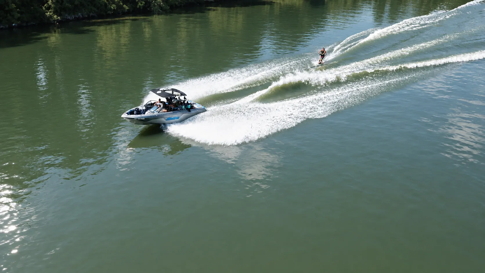 Drónfelvétel: motorcsónak húz egy wakeboardost a napfényes, zöld Tiszán